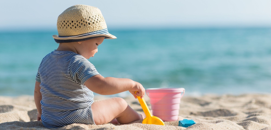 Kleinkind spielt am Strand mit Schaufel und Eimer im Sand
