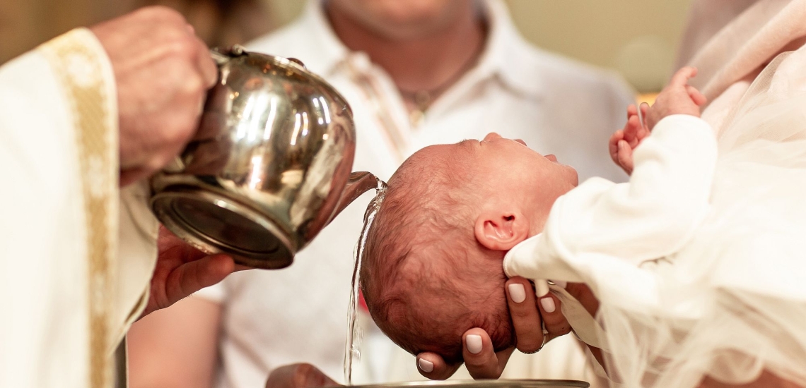 Priester gießt Baby bei Taufe Wasser über den Kopf