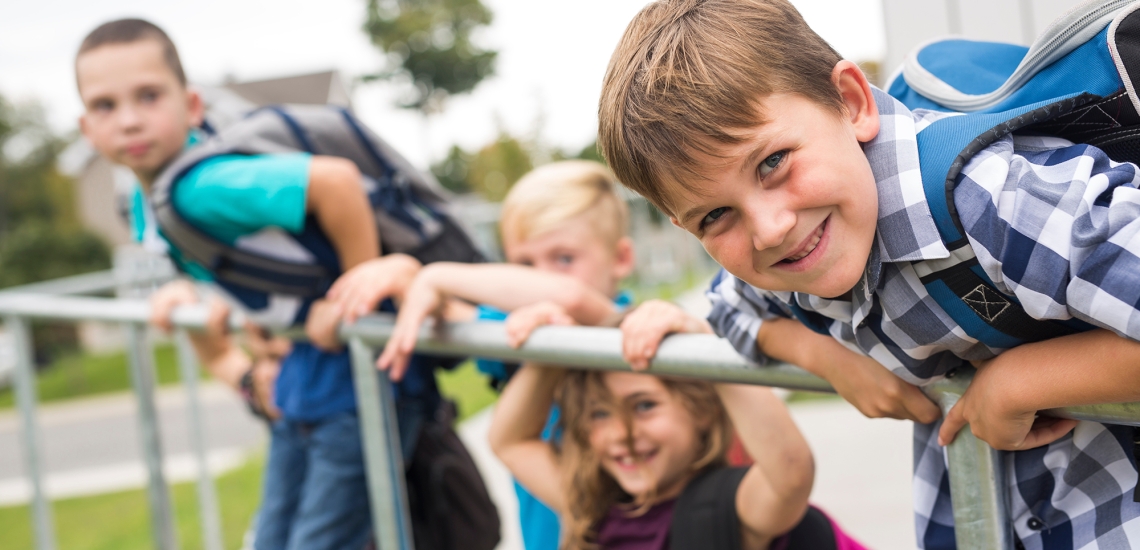 Vier Kinder spielen fröhlich am Geländer vor der Schule.