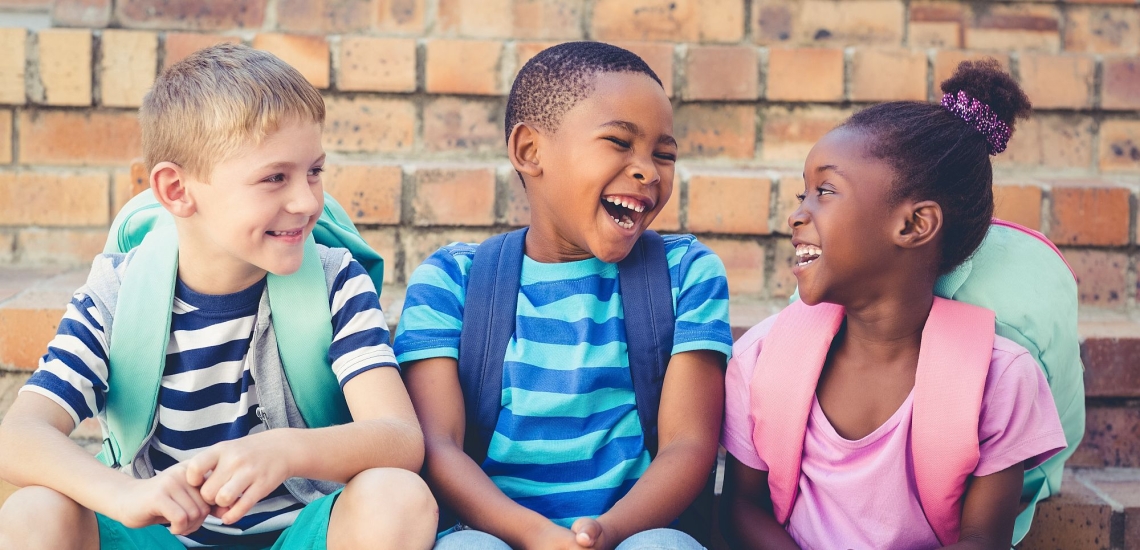 Drei Kinder sitzen nebeneinander und lachen 