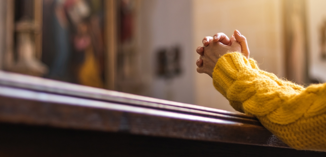 Eine Frau betet in einer Kirche. Es sind nur ihre gefalteten Hände zu sehen.