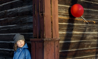 Etwa neun Jahre altes Kind schaut skeptisch auf einen roten Luftballon