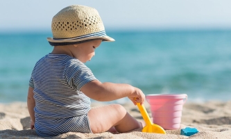 Kleinkind spielt am Strand mit Schaufel und Eimer im Sand