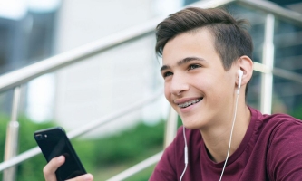 Jugendlicher sitzt lächelnd auf Treppe mit Smartphone und Kopfhörern